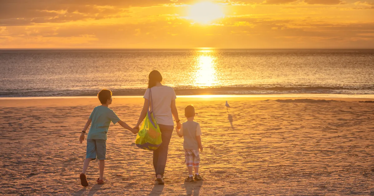 夕暮れの海辺を子どもと一緒に歩く親子の後ろ姿