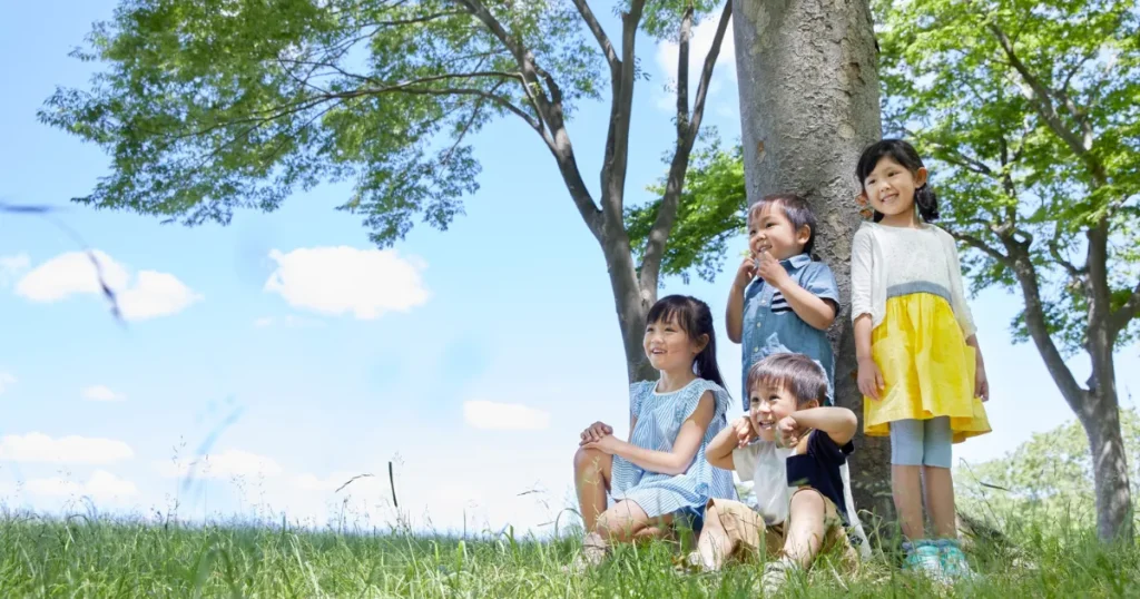 青空の下、木陰で笑顔を見せる4人の子どもたち