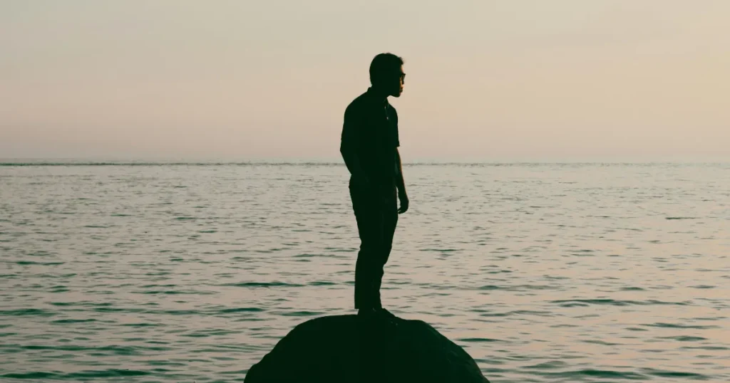 海辺に一人で立つ男性のシルエット|孤独や思索を感じさせる夕暮れの風景